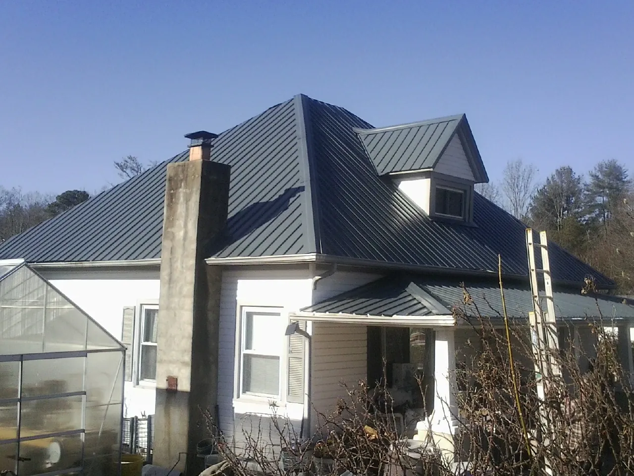 Dark blue standing seam metal roof on a white farmhouse with dormer in Fountain Green