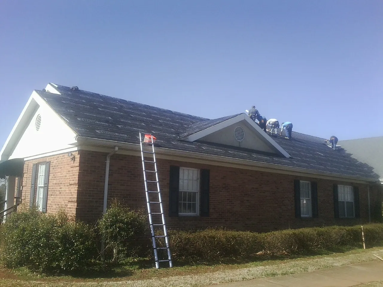 Crew tearing shingles off a brick ranch roof with a ladder set — Emergency Roof Repair work by our crew in Fountain Green
