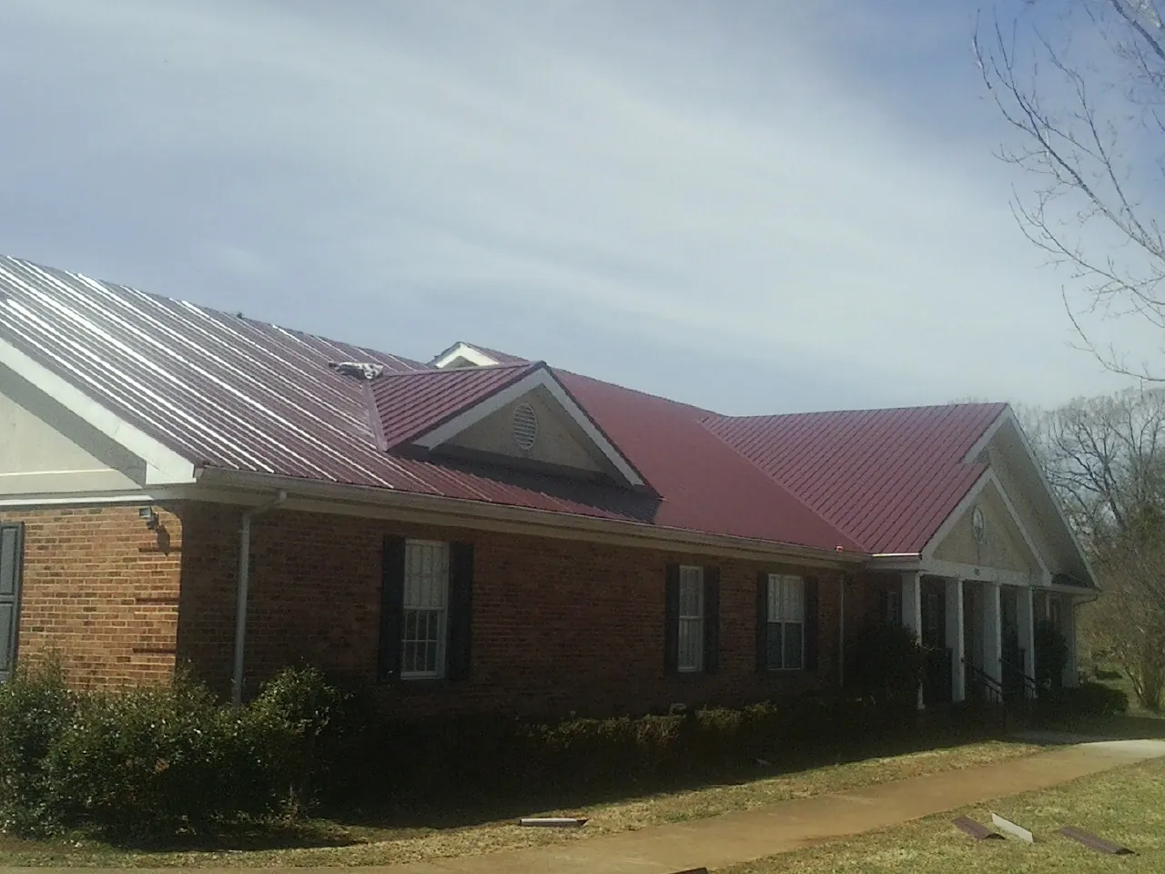 Red metal roof with gabled entries on a long brick building, from a Hail Damage Roof Repair job in Fountain Green