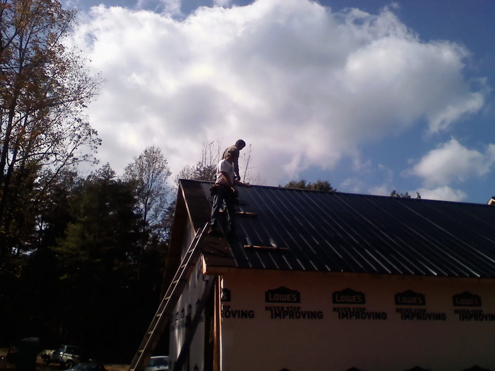 Roofer fastening dark metal panels high against a cloudy sky, from a Roof Inspection job in Fountain Green