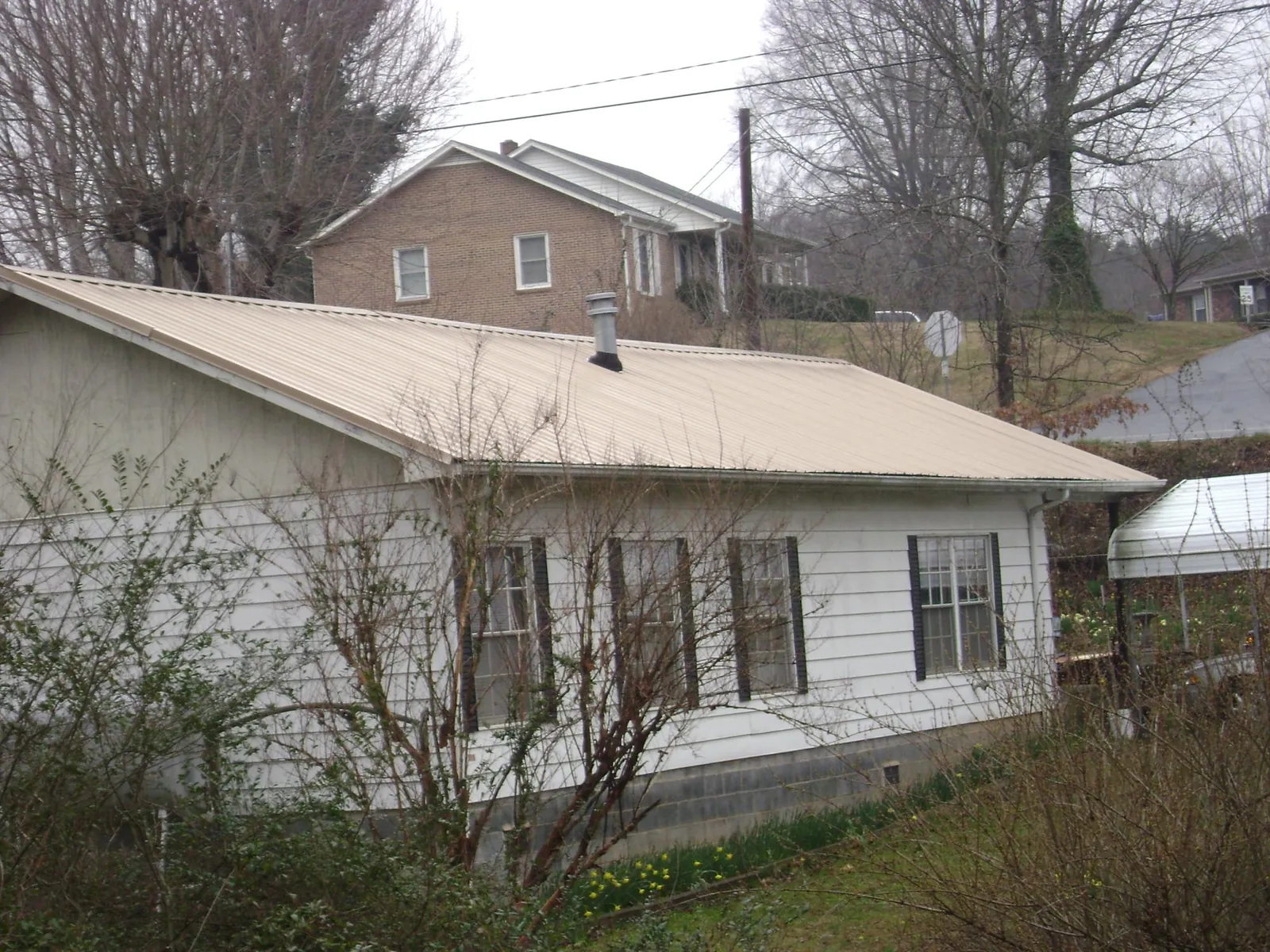 Tan metal roof on a white sided house set into a hillside — Commercial Roofing by Roofing Brothers in Fountain Green